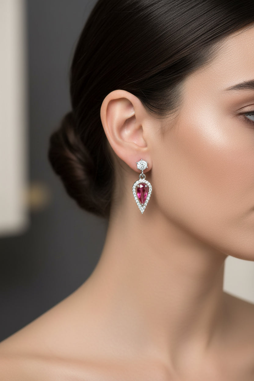 Heart-shaped earrings with red gemstones held in a hand against a white background